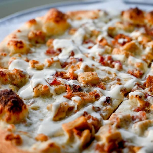 Close-up of a white pizza topped with chicken, bacon, and a creamy white sauce.