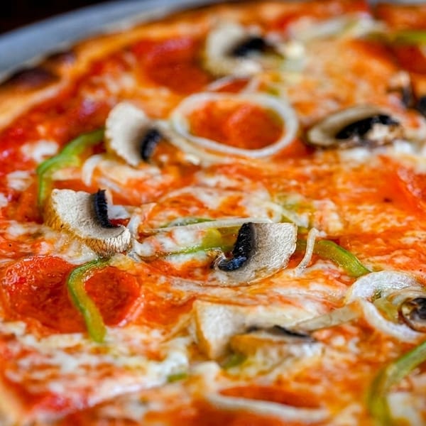 Close-up of a freshly baked pizza with pepperoni, mushrooms, green peppers, and onions.
