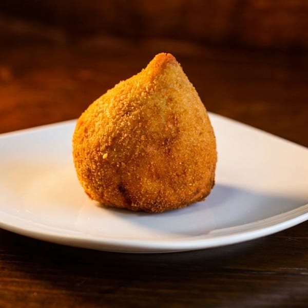 A golden-brown coxinha, a Brazilian fried chicken croquette, sits on a white square plate.